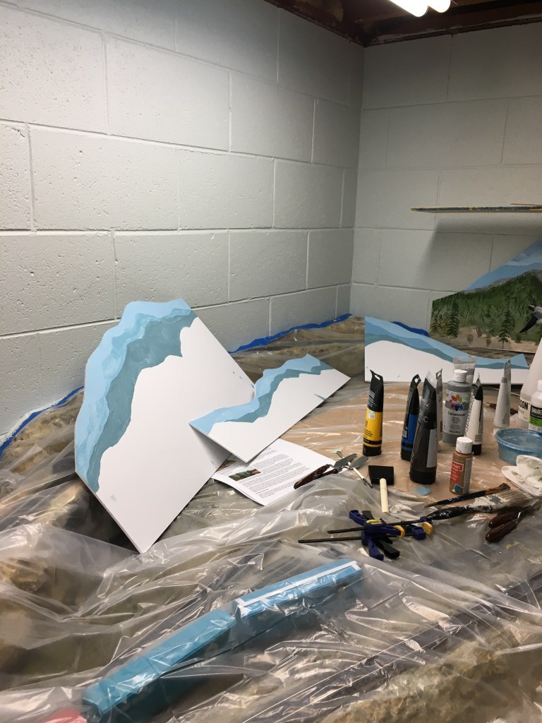 Sky is painted blue, mountains painted lighter shades to indicate distance.