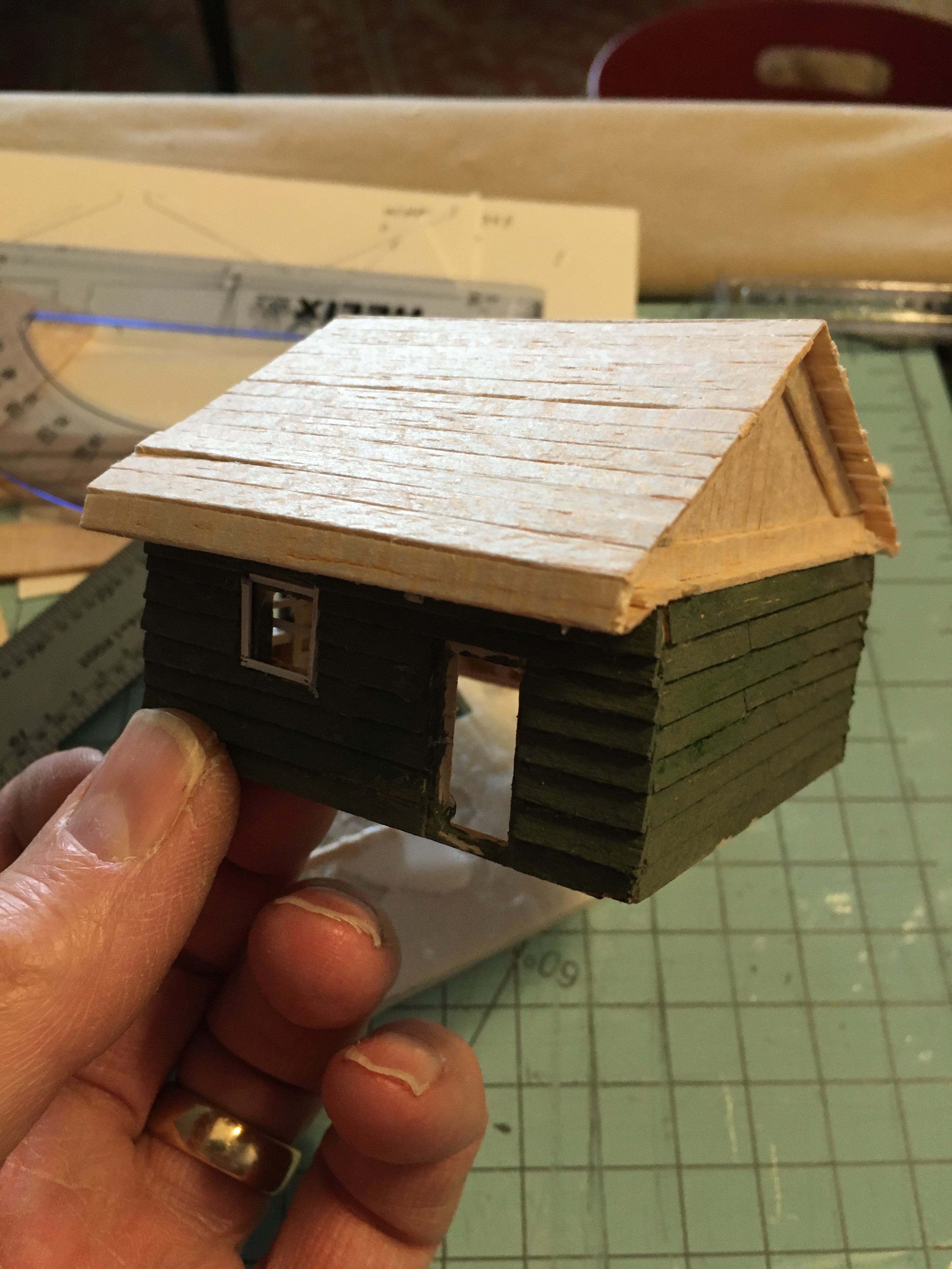 Green cabin showing overlap siding and windows with trim in place. Roof still needs painting.