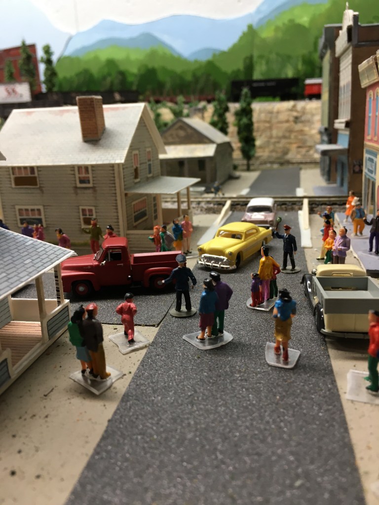 People are gathered at the intersection of Main and First Streets for a parade.