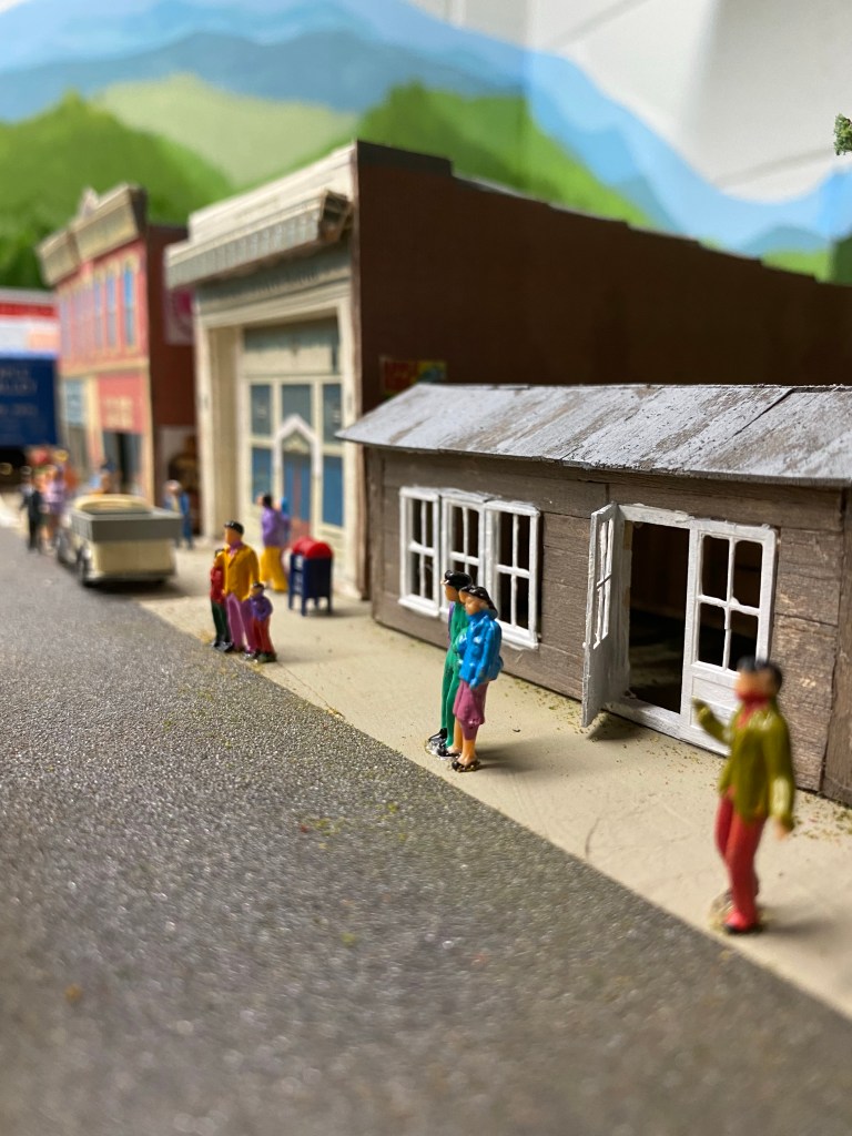 Several people standing along street in front of buildings.