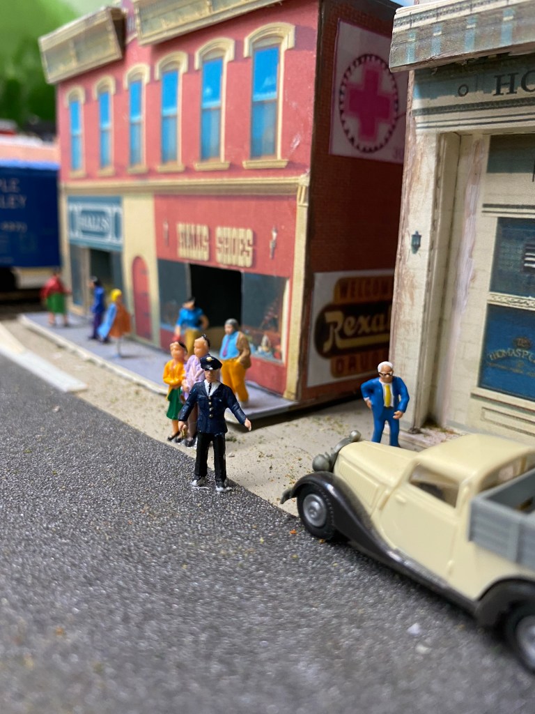 People in front of buildings, car, box car.