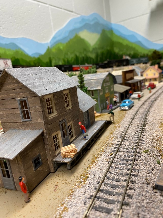 Several buildings on street along track, people working, cars.