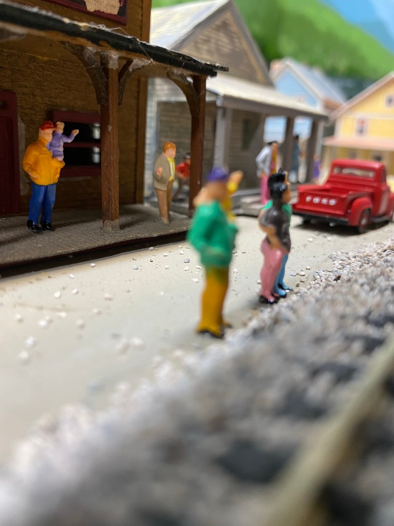 People standing on porches and near tracks, red truck.