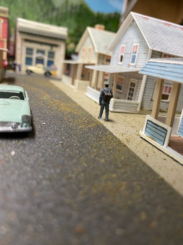 Mailman walking in front of houses, cars on the street.