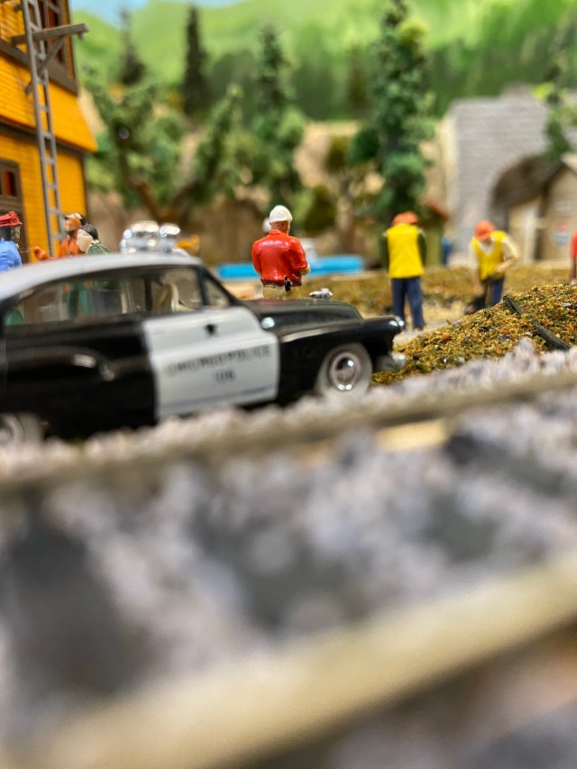 A police car just beyond tracks, men working.