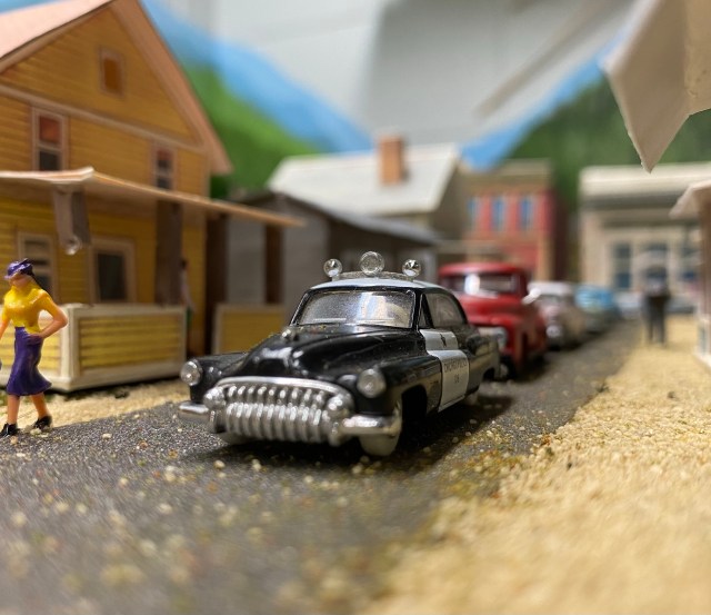 Woman walking, houses, police car, red truck, other cars