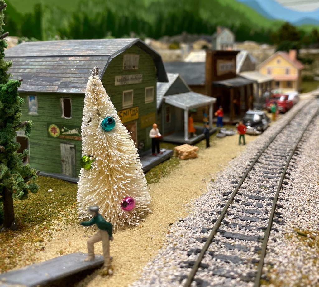 This is a lovely scene on the Maple Valley Short Line Model Railroad.  Smith's Supply, is near the new Christmas tree.  Folks are busy on a sunny day.  And as usual, the Ya'll Sit Cafe is full of happy patrons.