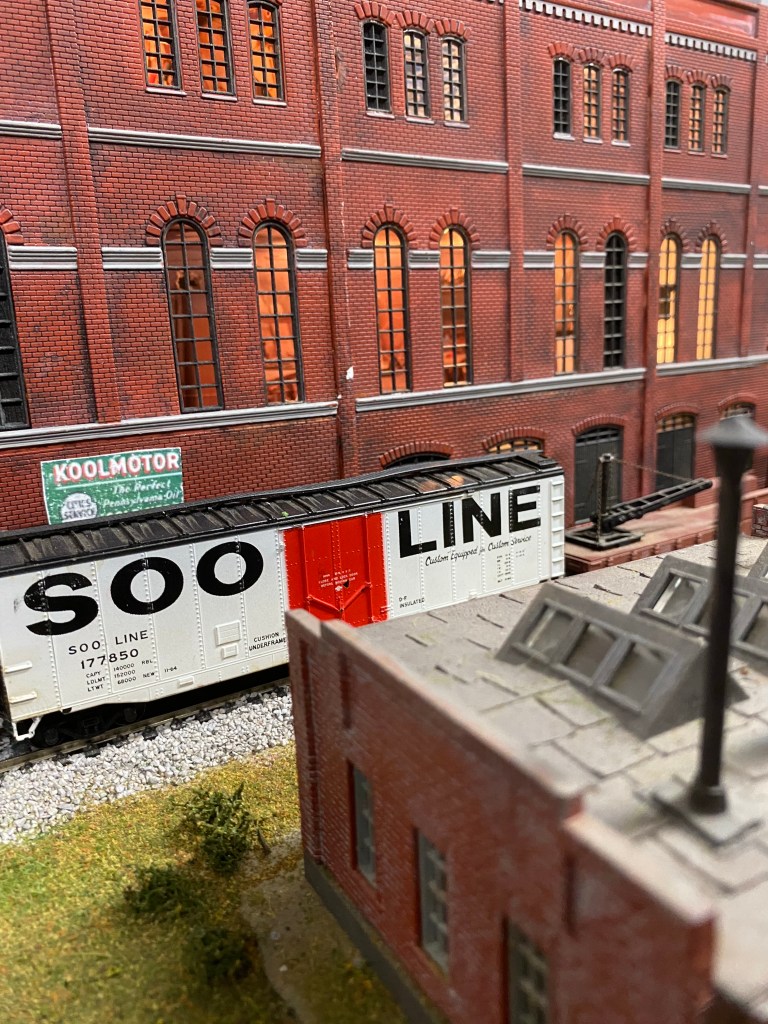 A small factory in front of the track, with the box car in front of Maple Valley Manufacturing Plant.