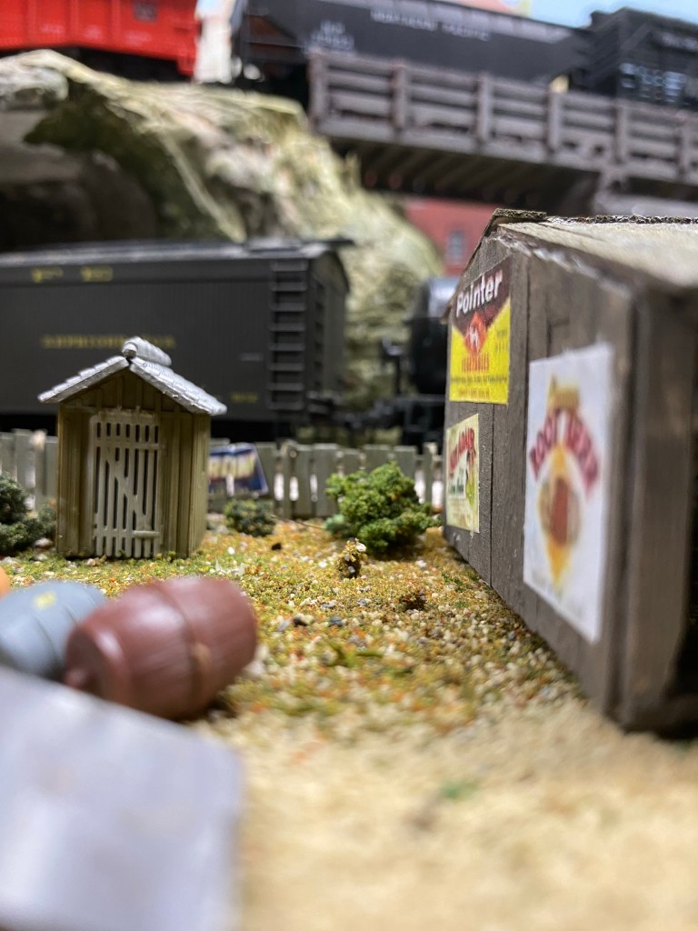 A close photo of a shed, barrels, two trains, and a wall of posters.