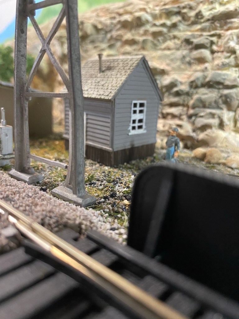 A detailed view of a small work shed, a man, the legs of a signal bridge, and part of an iron bridge.