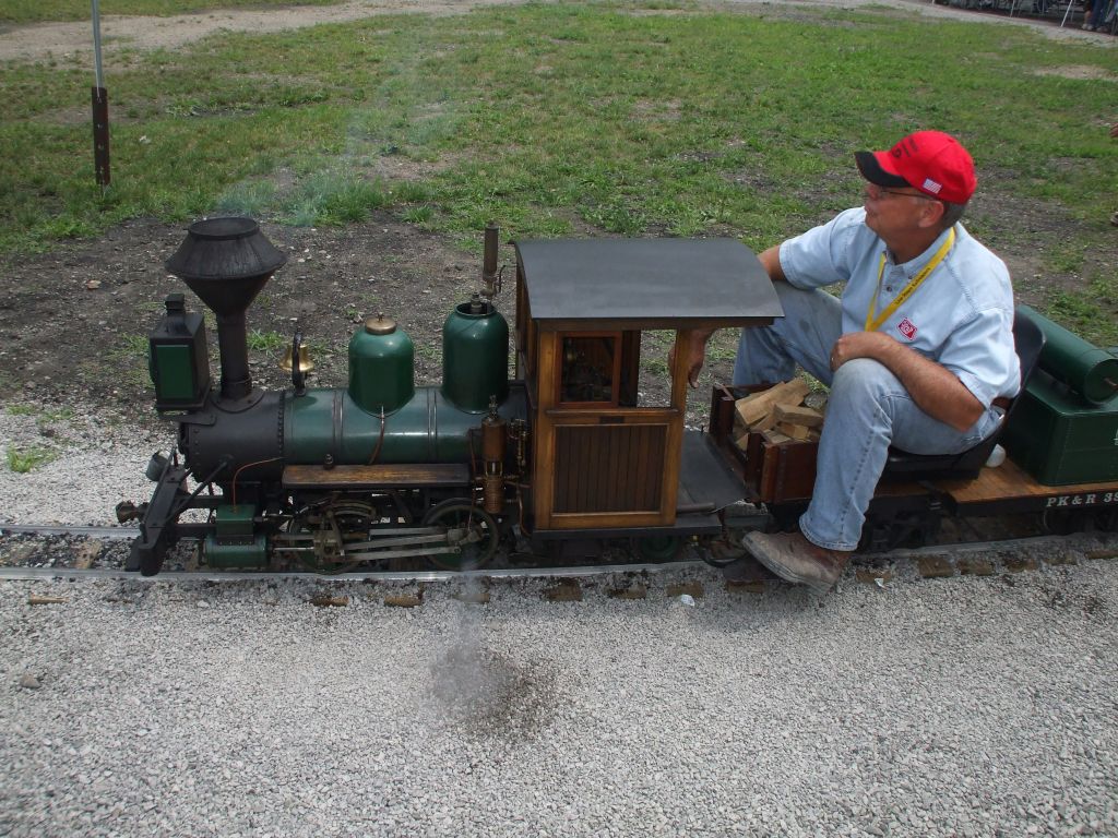 A miniature steam locomotive rolls out of the station with a load of passengers.