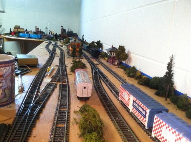 Four tracks, trees, train cars, buildings.