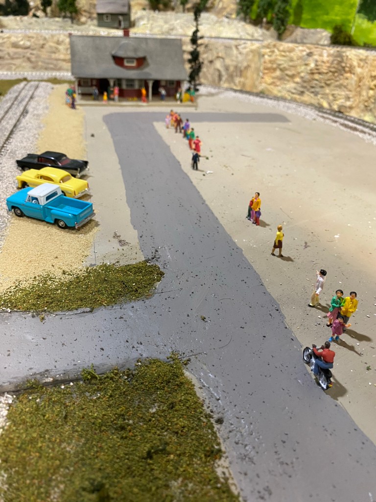 Gray painted road, cars, track, train station, people