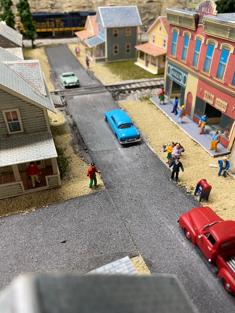 Two streets, cars, buildings, people, grade crossing with vehicles.