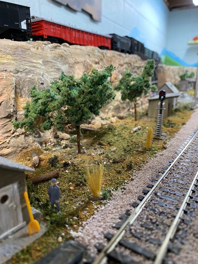 Small shed, man walking, trees, ground cover, signal, train