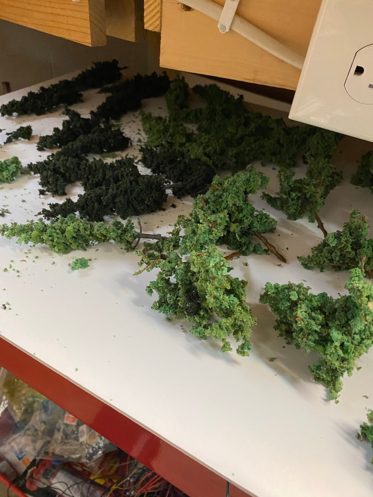 Several HO scale trees, a supply tray, wood panel