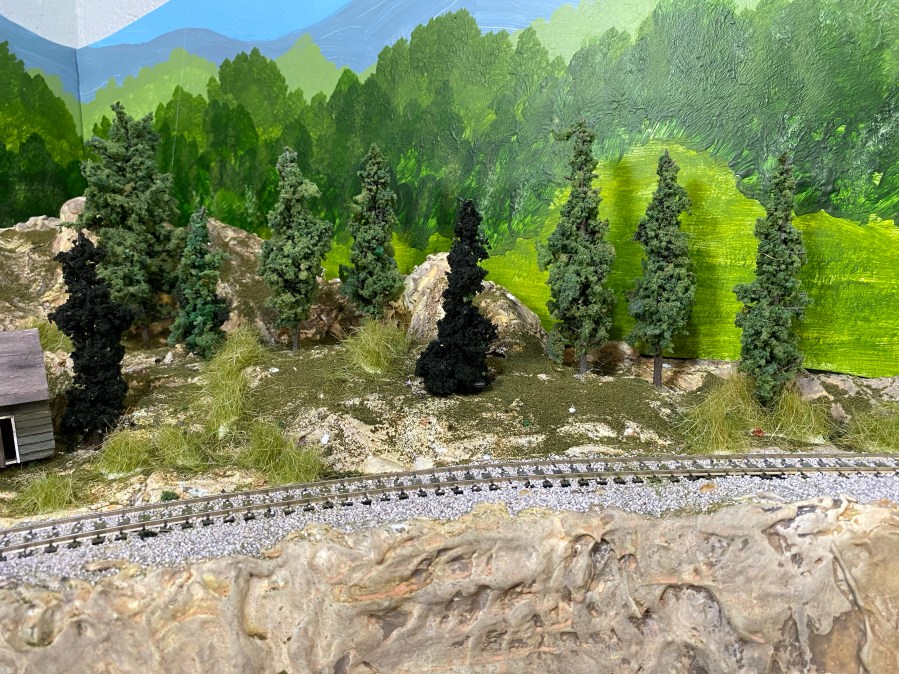 HO scale curved track, pine trees, forest backdrop, rocky terrain