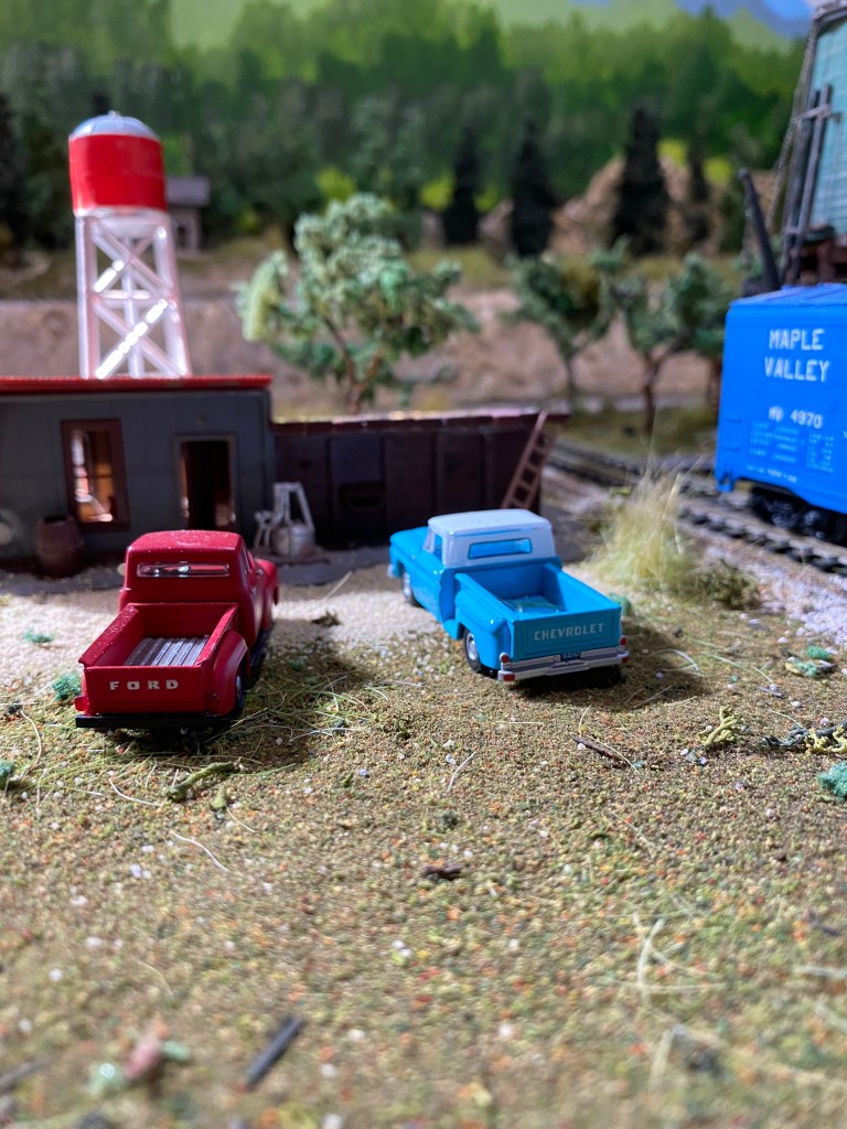 A blue and red pick-up truck, a workshop, water tower, and box car from Maple Valley