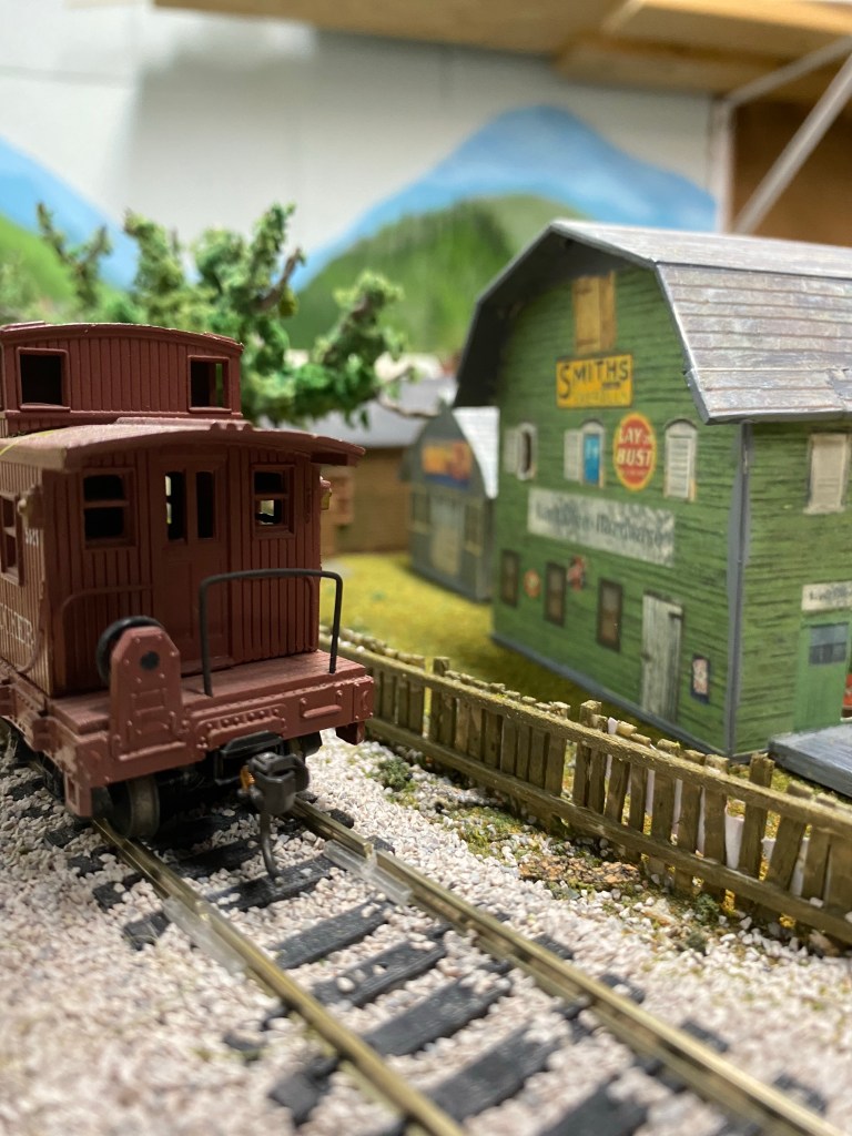 Red caboose, fence, green barn-shaped building, trees