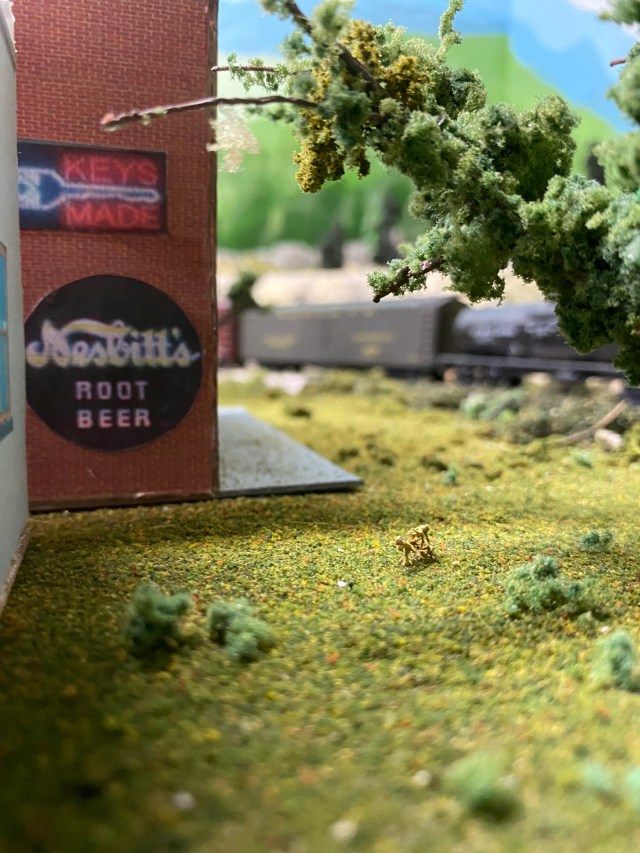 Building with posters, grass, tree branch, train passing