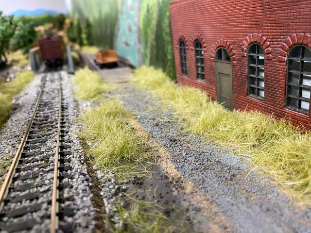 Trackside weeds, building, truck headed for New Town
