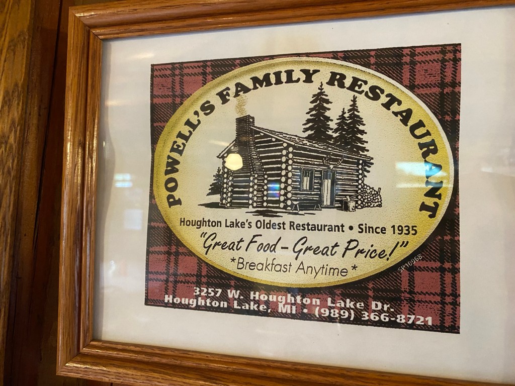 Picture of the log cabin Powell's Restaurant, plaid background, address, wood frame