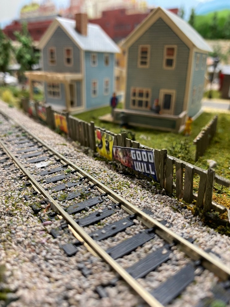 Track, fence, two blue houses, grass, people