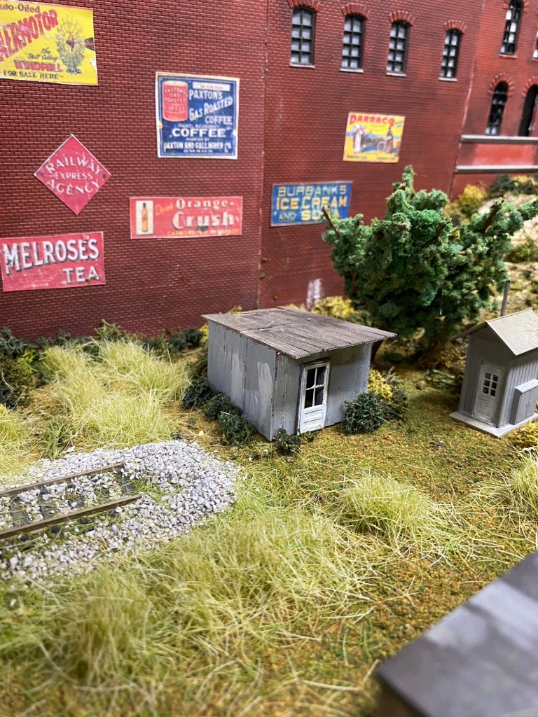 Factory wall, sheds, train track, weeds, trees