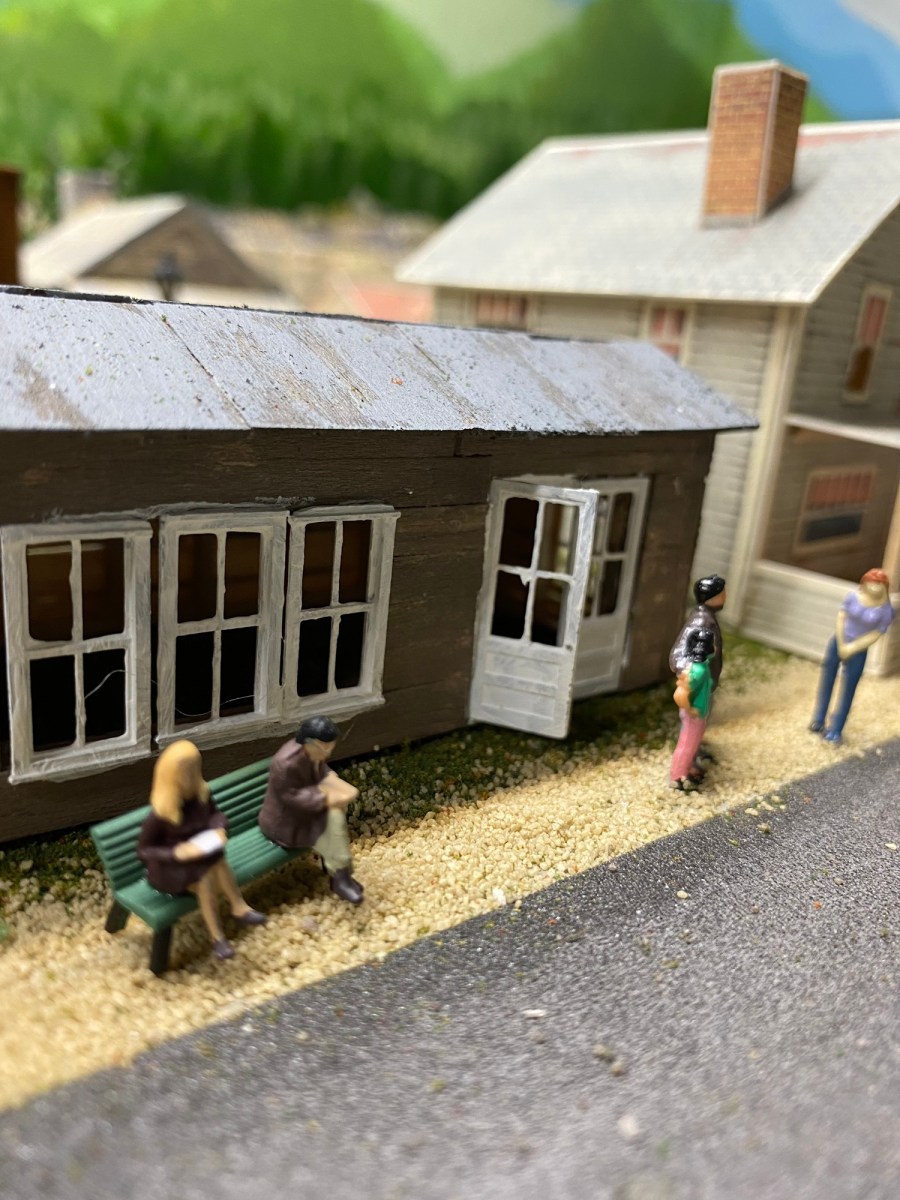 People sitting on a bench, people standing, shop, street, house