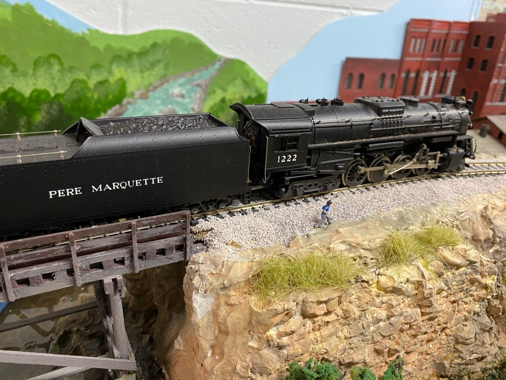 2-8-4 steam locomotive and tender, rocks, building, bridge
