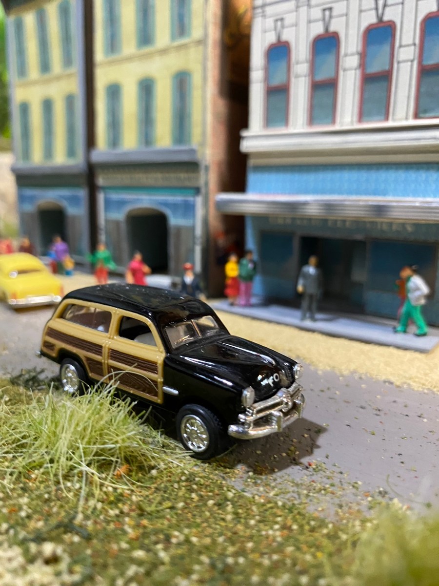 Ford Woody station wagon, weeds, buildings, people