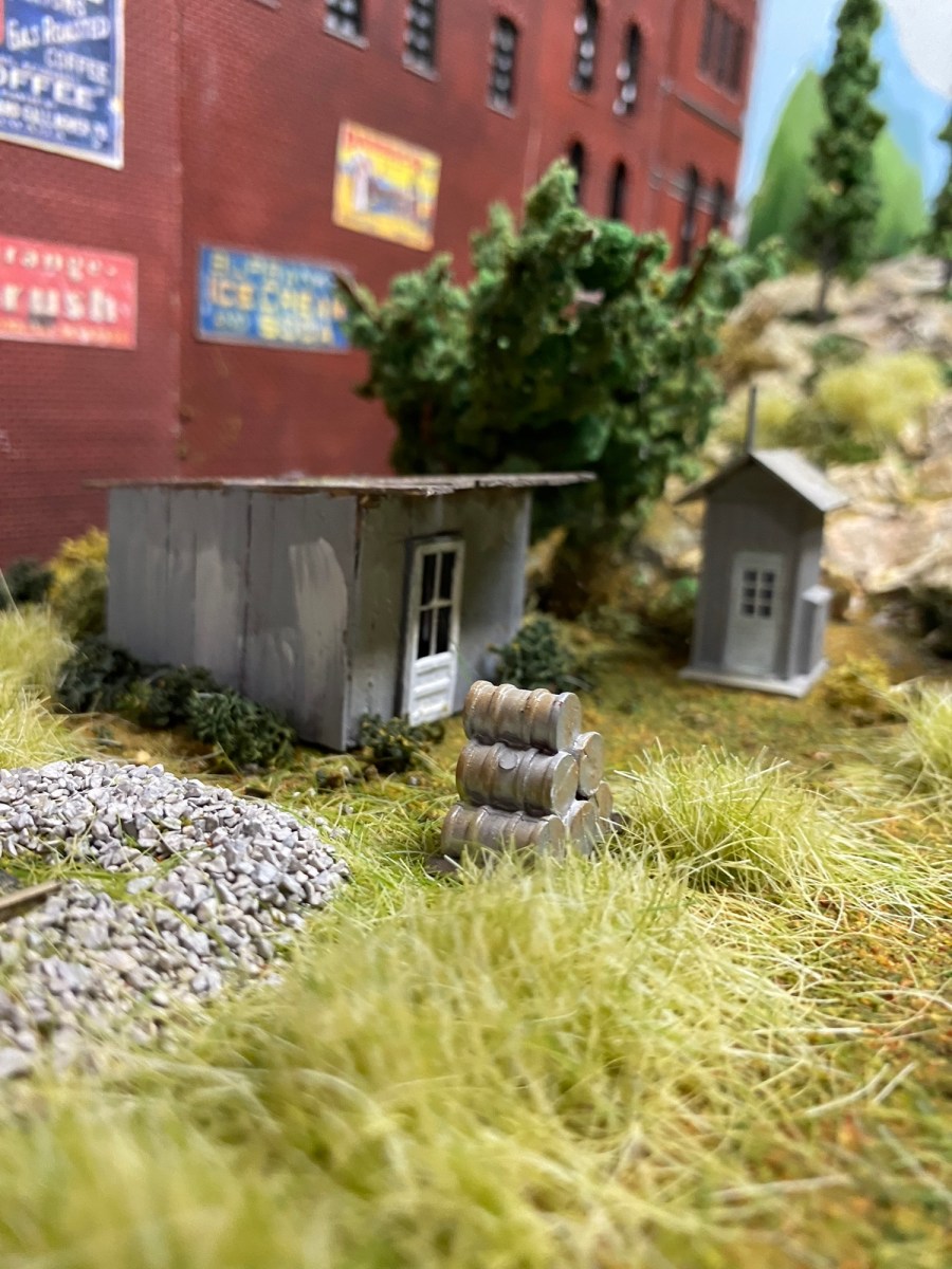 Gray sheds, weeds, rocks, tree, building