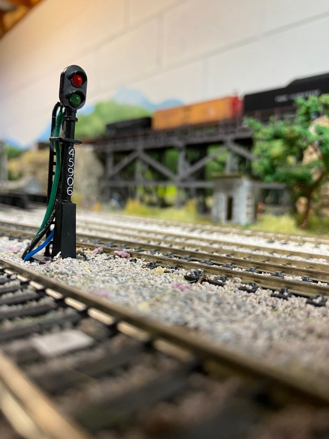 Trackside signal, tracks, trestle, train, trees, stones